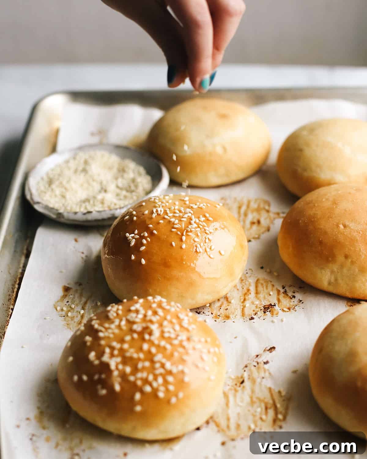 Sesame seeds sprinkled over homemade burger buns. front view of sesame seeds being sprinkled on Homemade Burger Buns