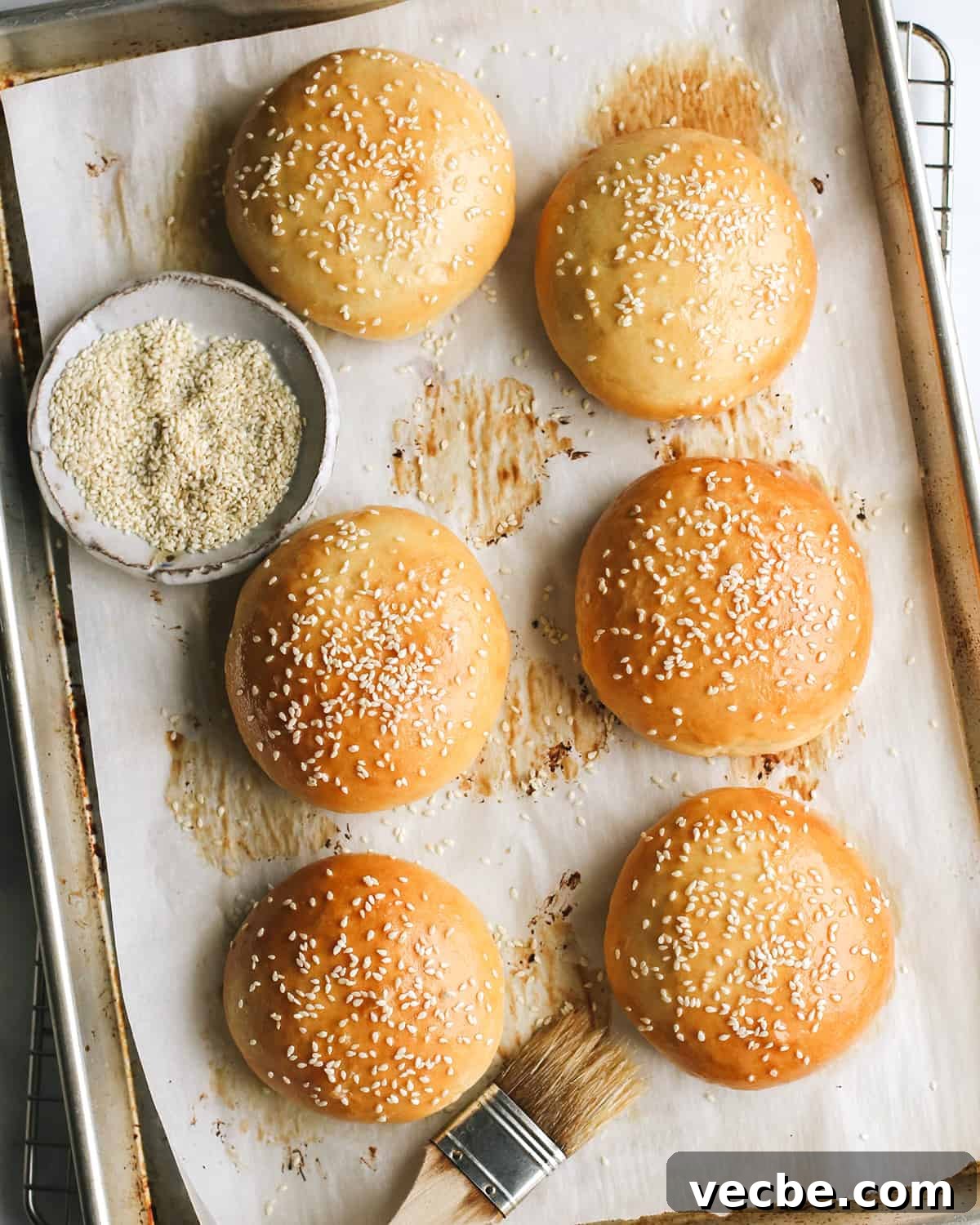 Homemade Hamburger Buns Recipe 5 6 Homemade Hamburger Buns on a baking sheet after baking topped with sesame seeds
