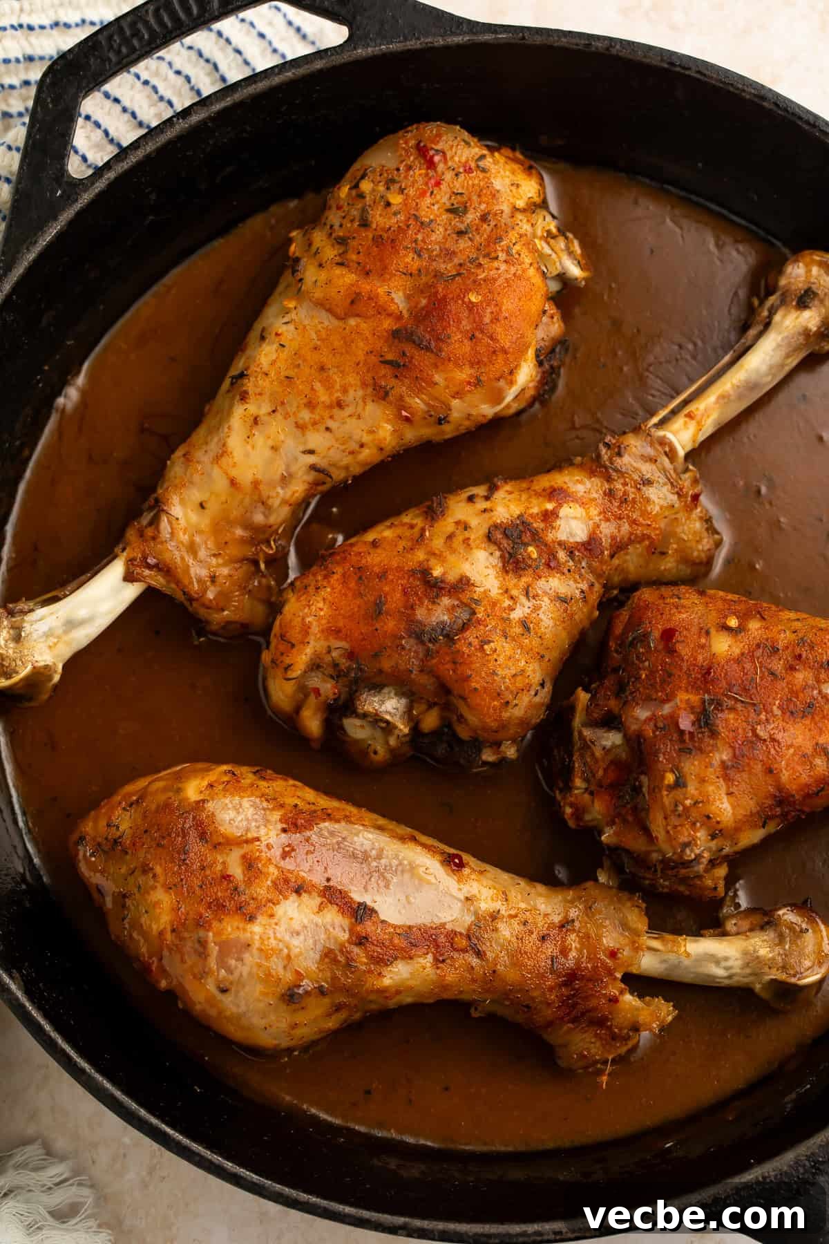 Juicy Oven Roasted Turkey Legs Recipe 4 Close up of four roasted turkey legs in a cast iron skillet of dark brown gravy.