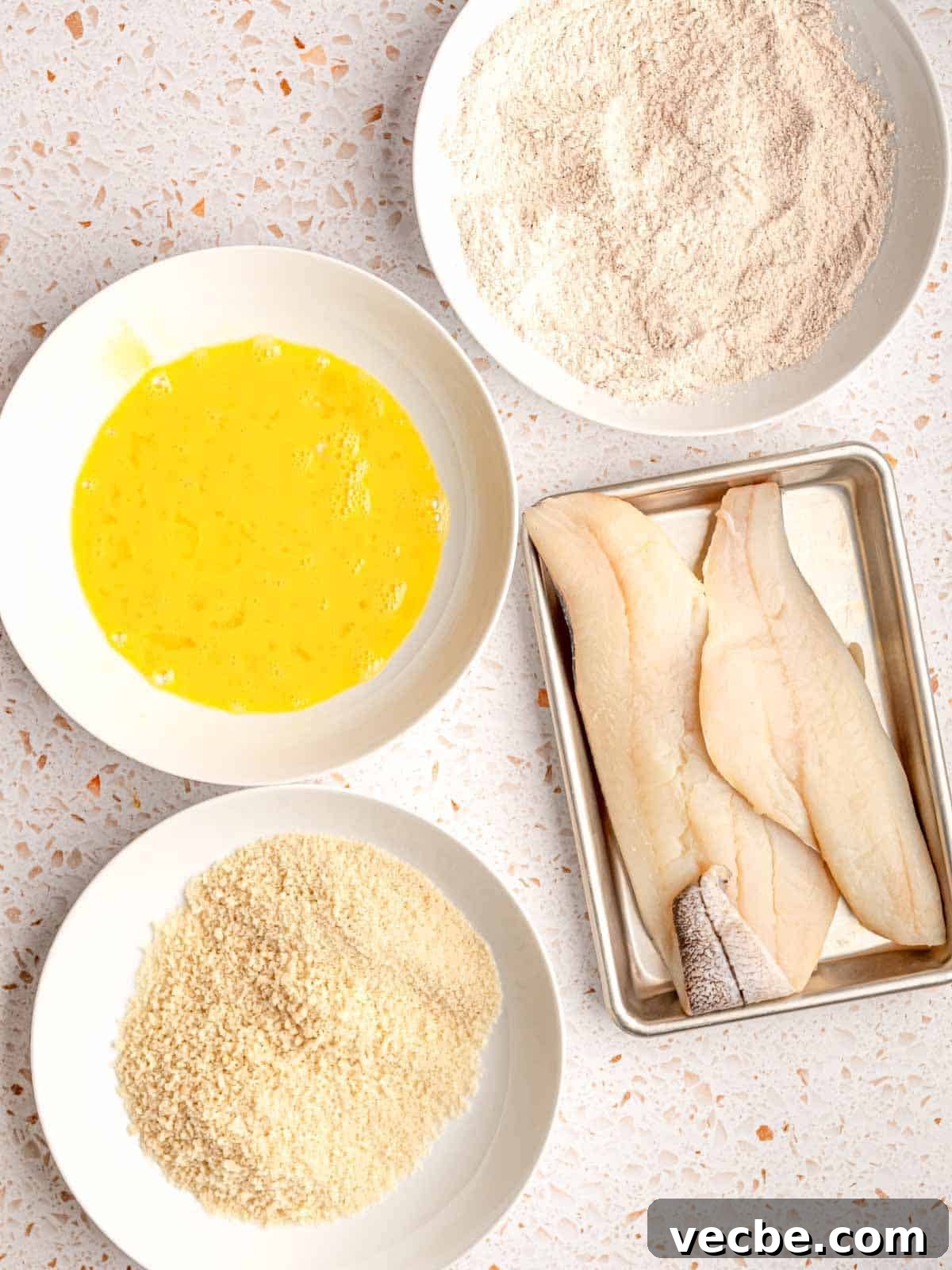 Crispy Fish Tacos with Fresh Mango Salsa Recipe 4 Fish on a metal tray next to bowls of flour, eggs and breadcrumbs.
