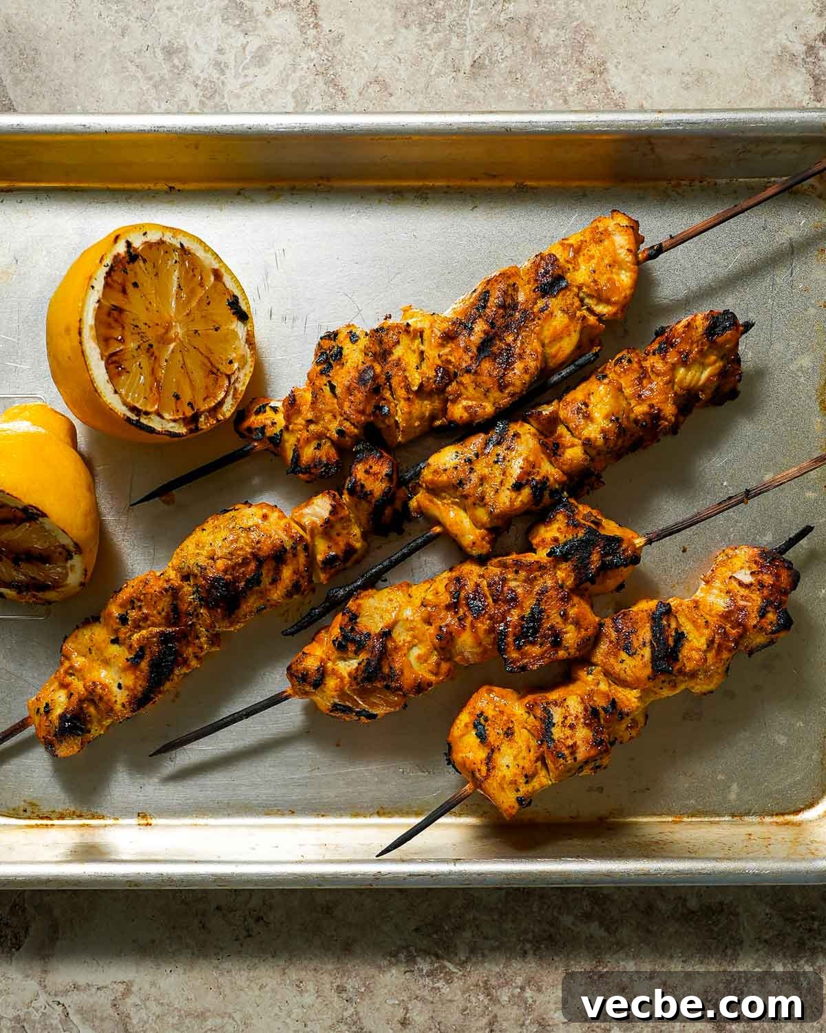 Yogurt-Marinated Grilled Chicken Skewers Recipe 6 Grilled skewers on a sheet pan with charred lemon.