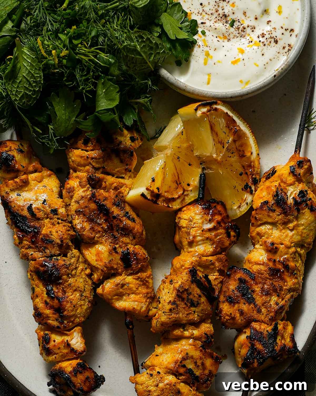 Yogurt-Marinated Grilled Chicken Skewers Recipe 7 A plate of grilled yogurt marinated chicken with a charred lemon, a small bowl of yogurt and herbs.