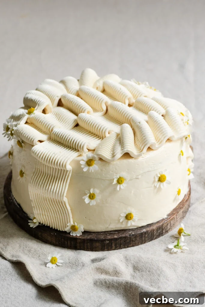 Moist Banana Layer Cake with Honey Buttercream Recipe 3 Frosted banana layer cake, decorated with edible flowers on a wood cutting board.