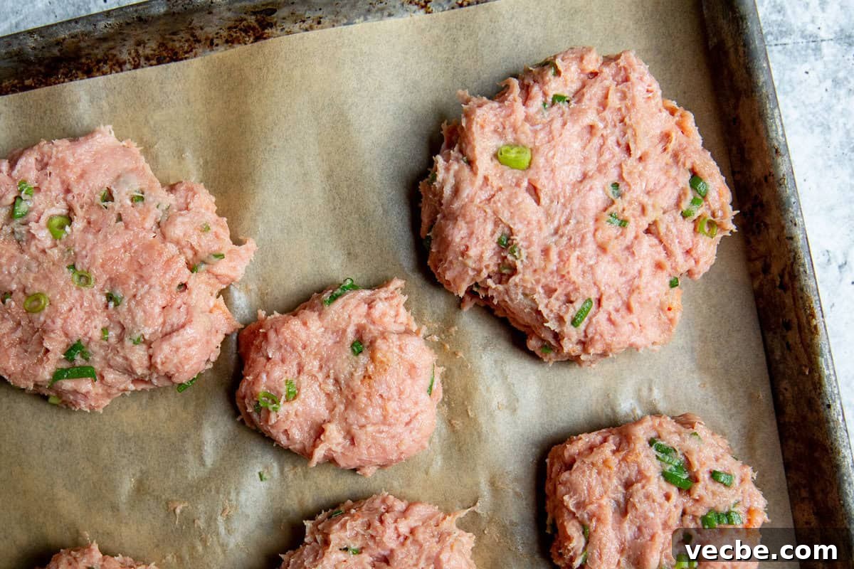 Banh Mi Burger Recipe with Sriracha Cream Cheese 5 raw bahn mi burgers on a parchment lined baking sheet.