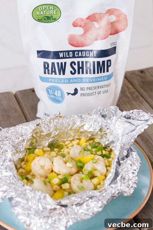 Caribbean Shrimp Foil Packets with Pineapple and Peppers 2 Foil Packet Caribbean Shrimp still in the foil on a blue plate with a bag of Open Nature Raw Shrimp in the background