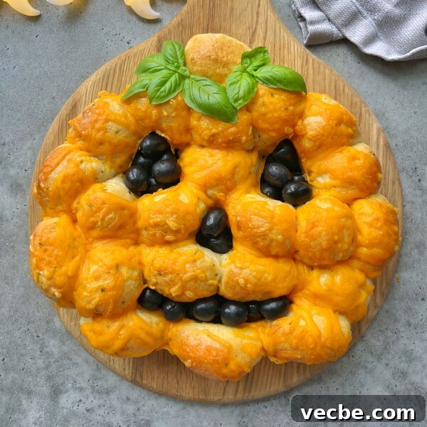 Spooky Halloween Appetizers to Wow Party Guests 5 Pumpkin-shaped pull-apart bread, topped with melted cheddar cheese and decorated with black olive bites for the face and fresh basil as a stem, is a fun dish to add to your collection of festive food recipes. Served on a round wooden board.