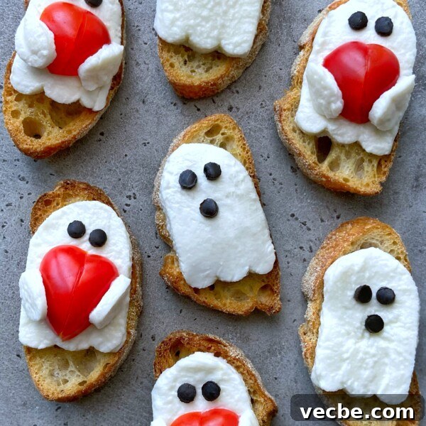Spooky Halloween Appetizers to Wow Party Guests 6 Slices of bread topped with mozzarella cheese ghosts—some holding red tomato hearts—all have olive piece eyes. These fun bites make a spooky addition to your food recipes and health-conscious dishes, arranged on a grey surface.