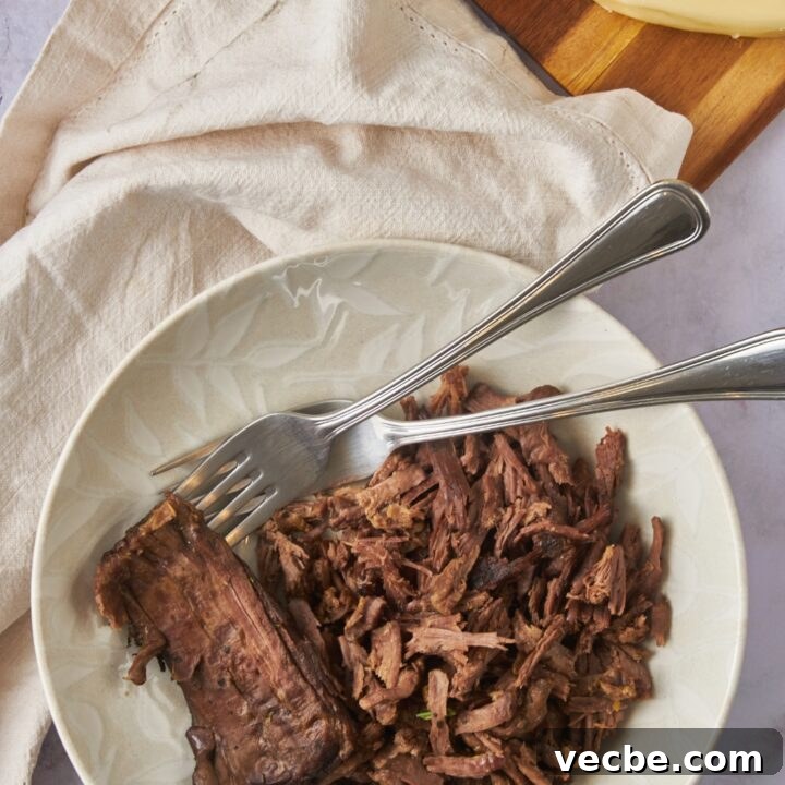 A bowl of cooked and shredded tri tip with two forks in the bowl.