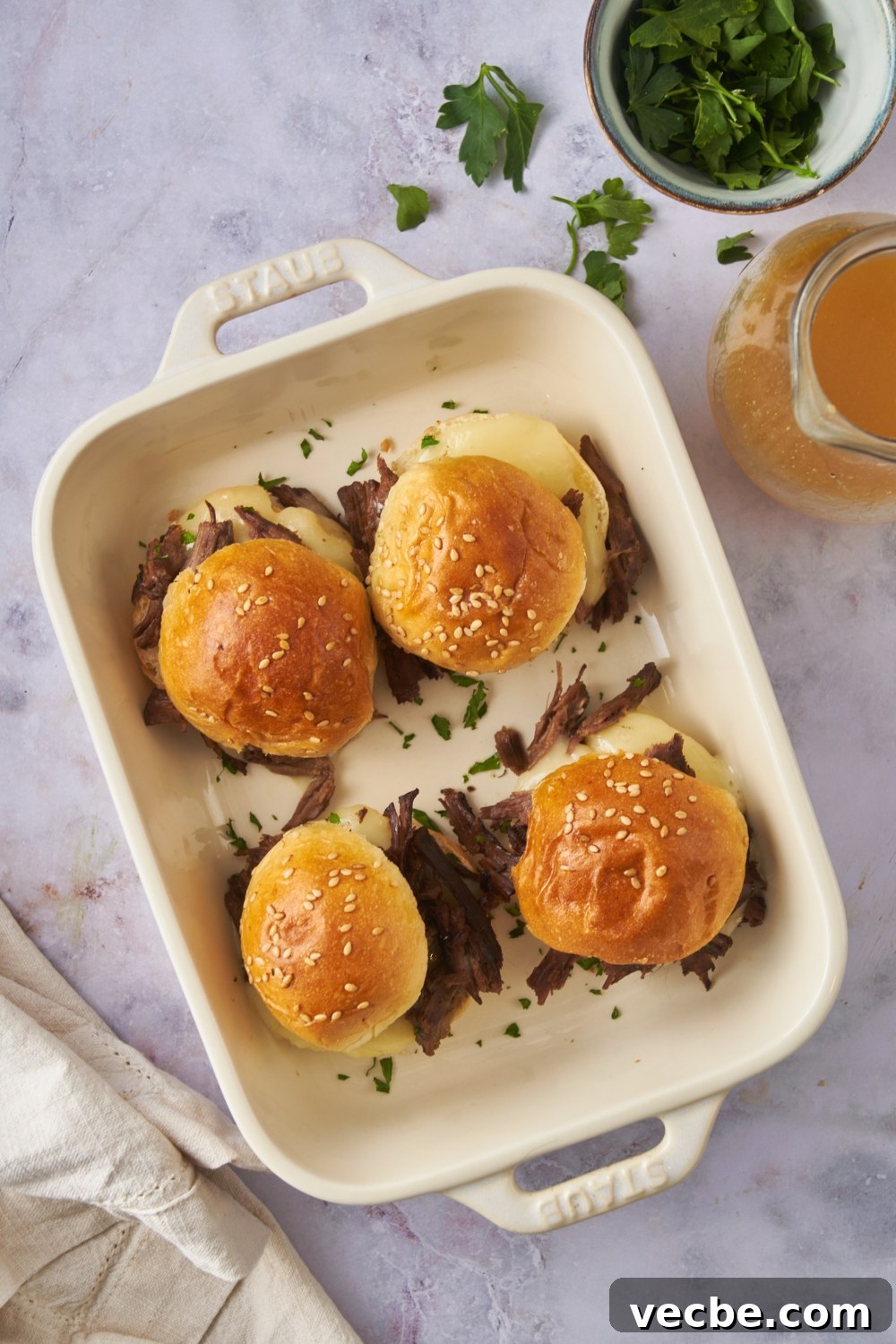 Fall-Apart Slow Cooker Tri-Tip Recipe 10 Overhead view of four mini tri tip sandwiches with cheese and fresh herbs in the sandwiches. Each sandwich is topped with a buttered poppyseed bun.