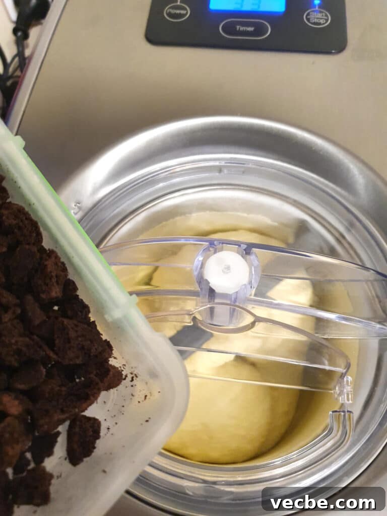 Cookies and Cream Ice Cream Recipe 15 adding crushed up Oreos to ice cream churning in churner.