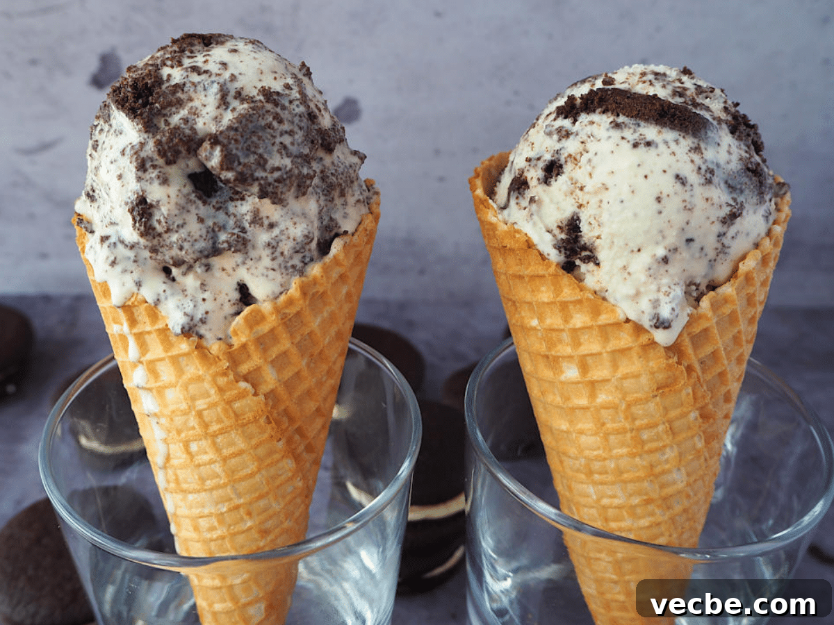 Cookies and Cream Ice Cream Recipe 21 Two waffle ice cream cones with a large scoop of cookies and cream ice cream in each, resting in glasses, with Oreos scattered around them.