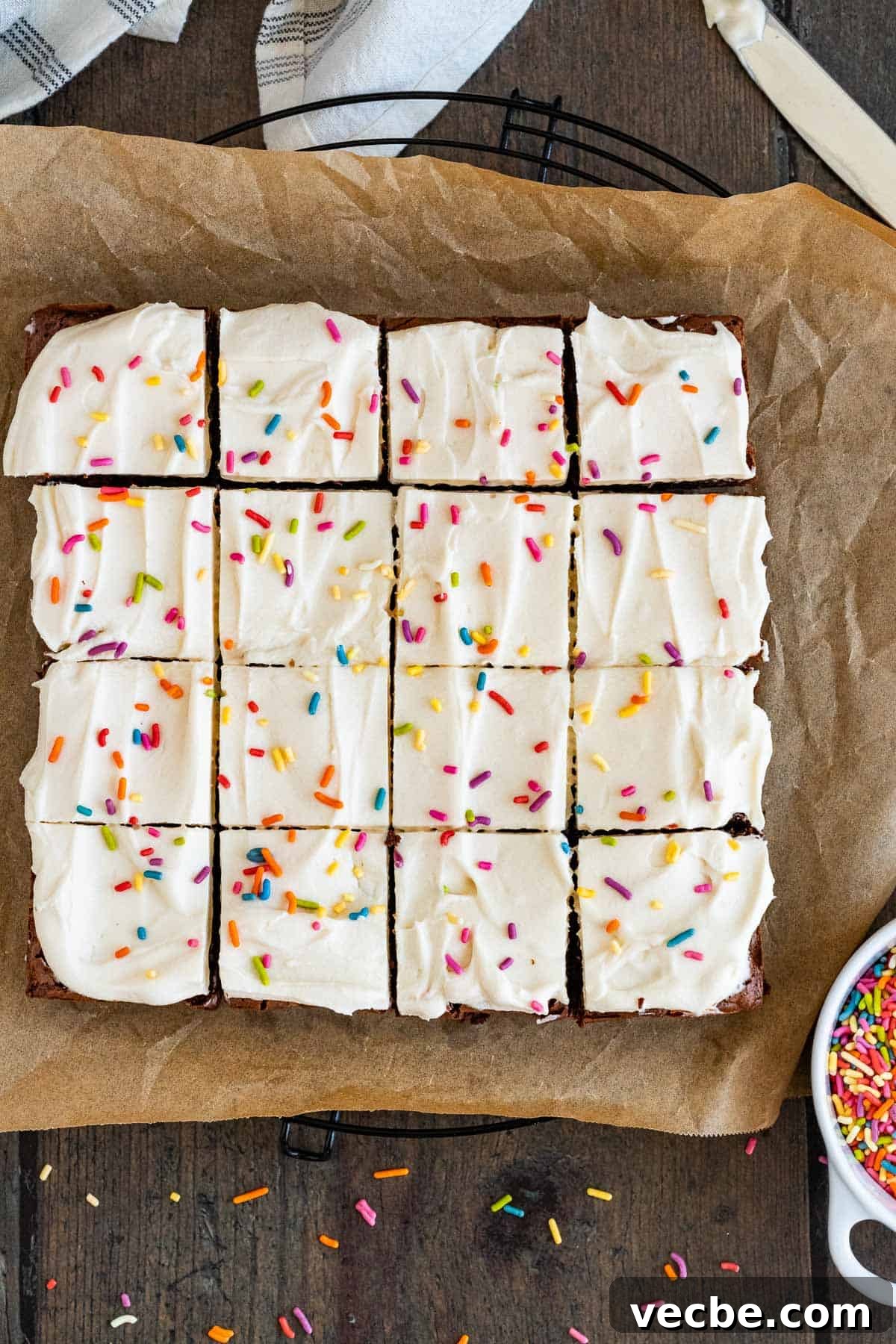 Chewy Brownies with Cream Cheese Frosting Recipe 3 Brownies with cream cheese frosting and sprinkles sliced into squares on parchment paper