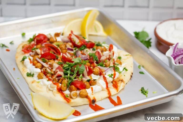 ¾ view of a sheet pan with Falafel-Spiced Chickpea Flatbread on top surrounded by garnishes.