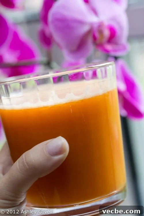 Hand holding a class of fresh juice with orchids in the background.