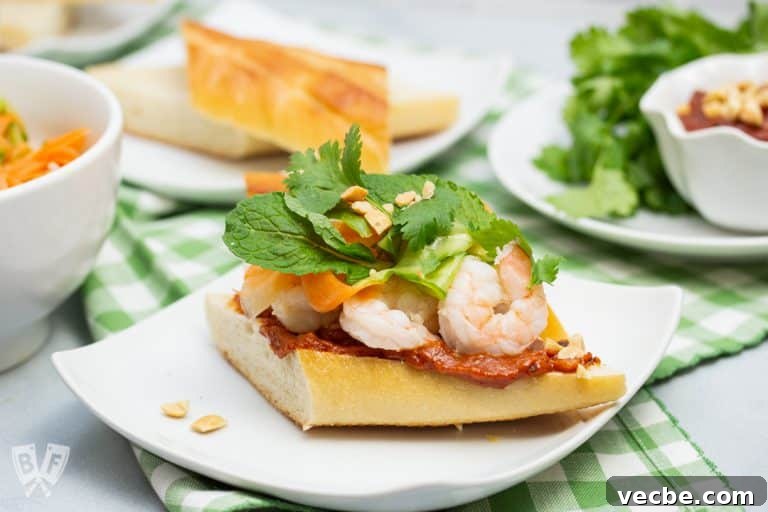 Vietnamese shrimp sandwich on a plate piled with pickled veggies, fresh herbs and peanut sauce.