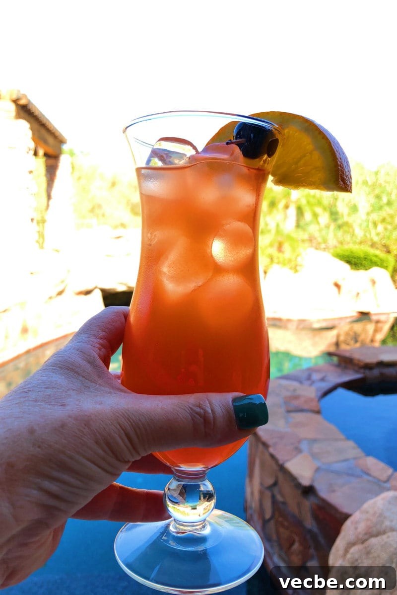 Hurricane Cocktail in a Glass hand holding a hurricane cocktail with a backyard in the background