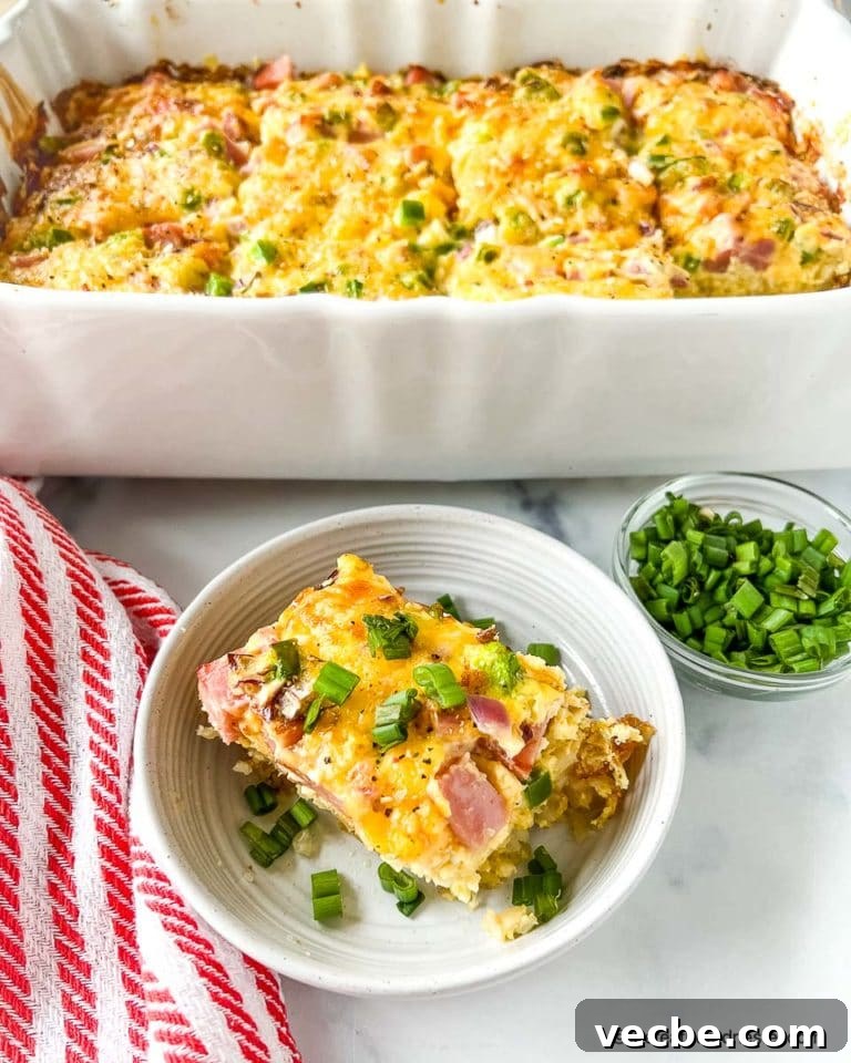 Serving of ham and tater tot casserole with the casserole dish in the background.
