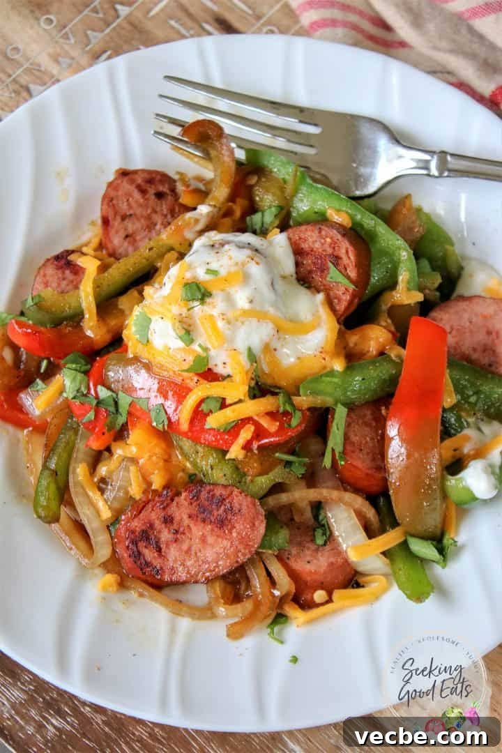 Authentic Cajun Sausage and Peppers Recipe 2 Keto sausage and peppers on a white plate garnished with sour cream and cheese and seasoned with Cajun spices
