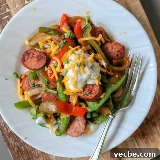 Authentic Cajun Sausage and Peppers Recipe 5 Cajun sausage and peppers served on a white plate and garnished with sour cream and cheese