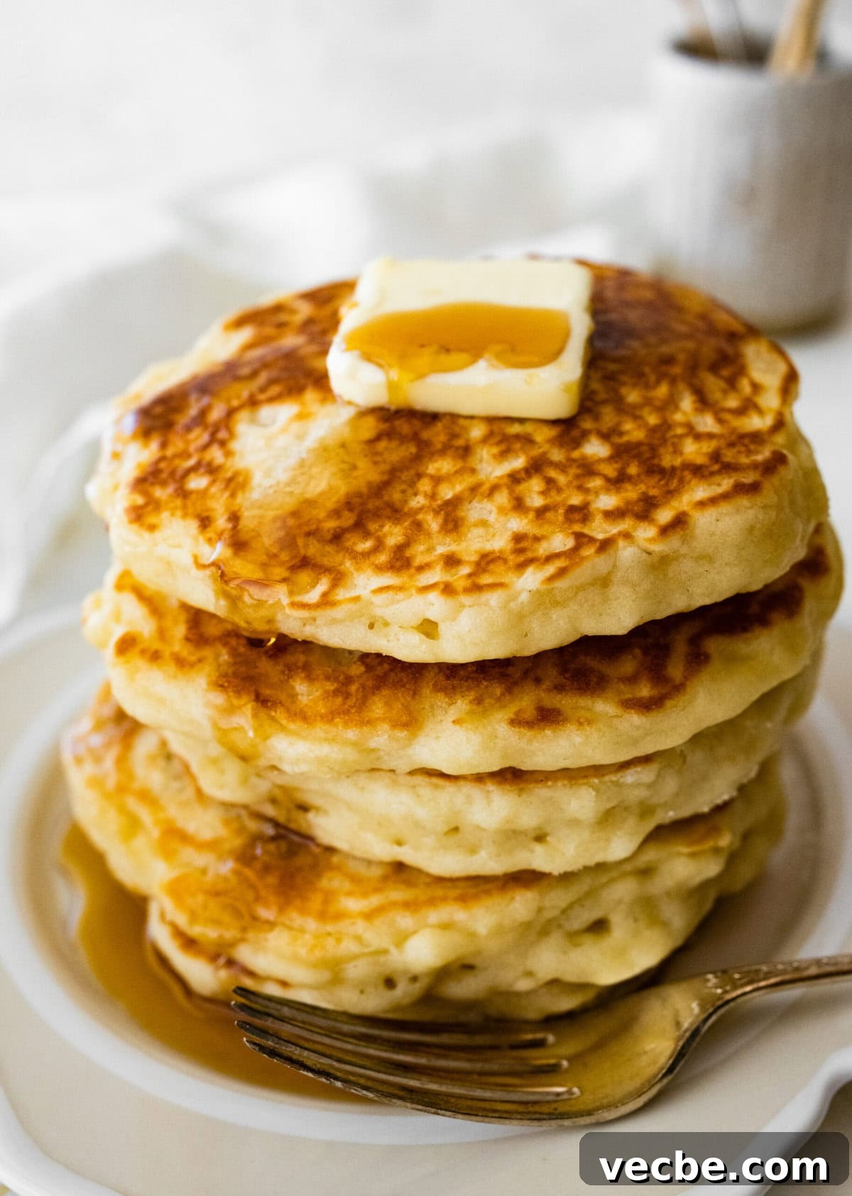 65+ Christmas Dessert Recipes Your Guests Will Love 29 a big stack of fluffy pancakes on a plate with butter on top. Pouring hot syrup on the top. A jug of milk visible in the background.