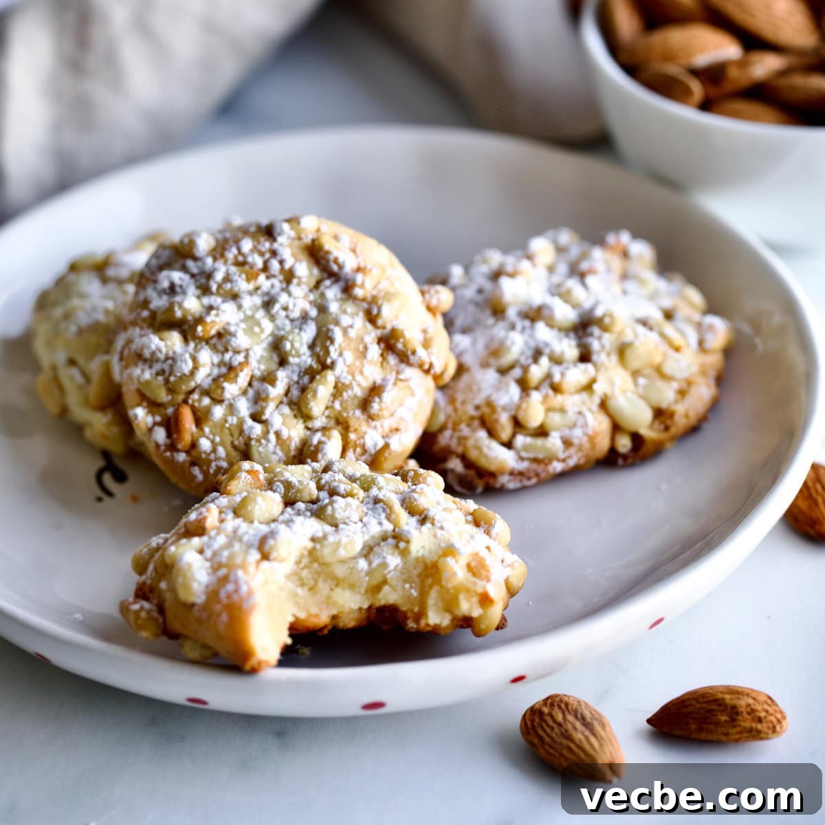 65+ Christmas Dessert Recipes Your Guests Will Love 4 Italian Pignoli Cookies, one of which is missing a bite, on a plate.
