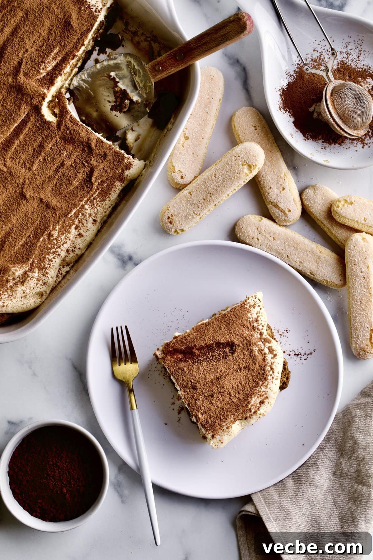 65+ Christmas Dessert Recipes Your Guests Will Love 37 slice of tiramisu on a plate with ladyfinger cookies in the background.