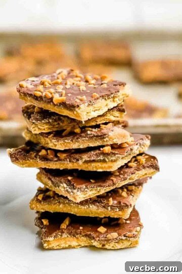 Seven pieces of christmas crack stacked on a white plate, with a tray of christmas crack behind it in a sheet pan.