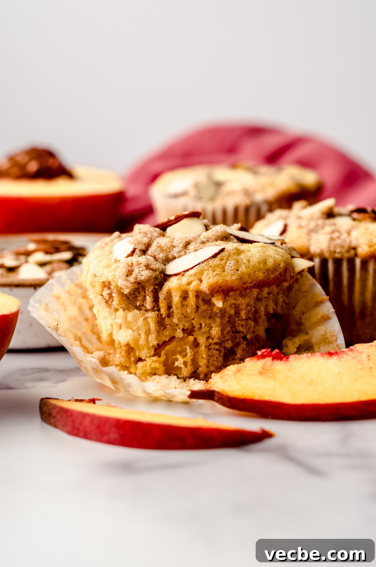 Peach Almond Streusel Muffins with Crumb Topping 2 A peach almond streusel muffin sitting on a surface with peaches and almond slices around it.