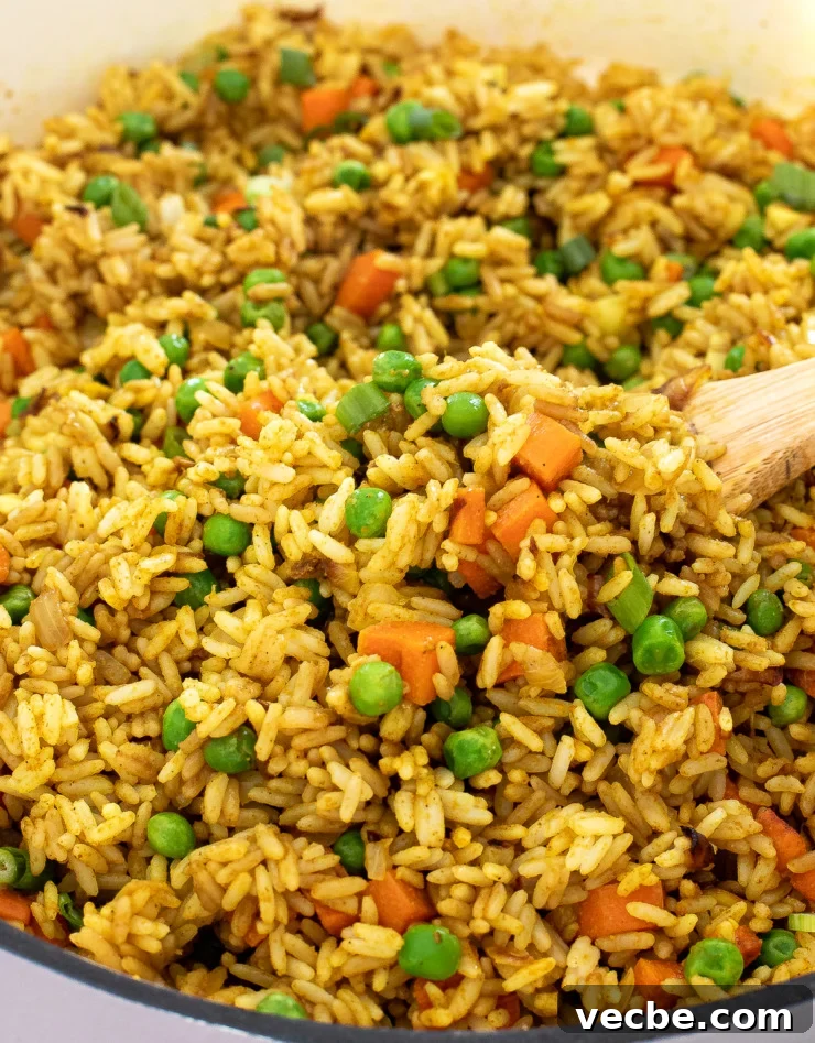 Fragrant Curry Fried Rice Recipe 3 Fried rice in a skillet with a wooden spoon scooping a portion out.