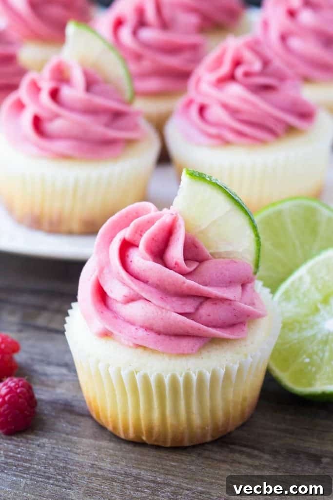 Zesty Lime Cupcakes with Raspberry Buttercream 3 One lime cupcake with raspberry frosting and a plate of cupcakes in the background. Garnished with lime slices and raspberries.