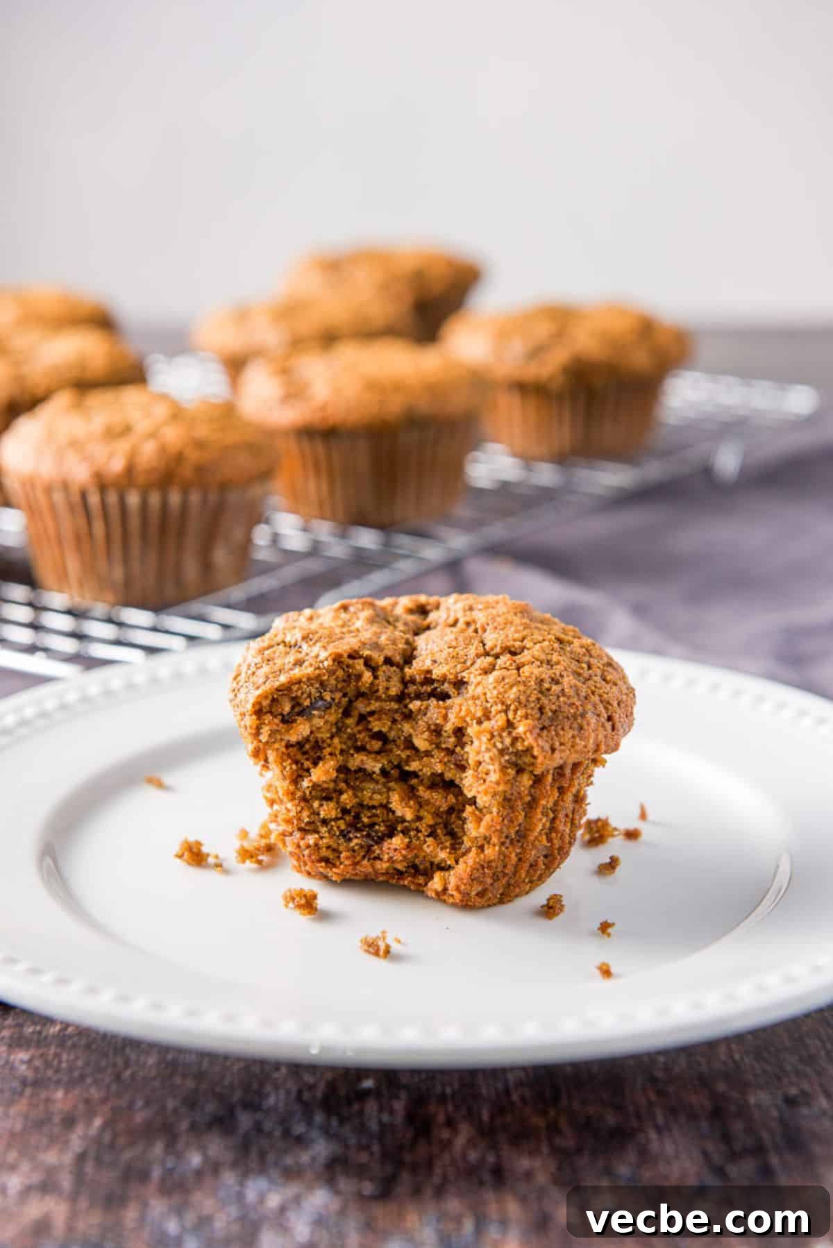 Moist Raisin Oat Bran Muffins Recipe 2 A white plate with a bite out of one of the oat bran muffins. There are more muffins in the back