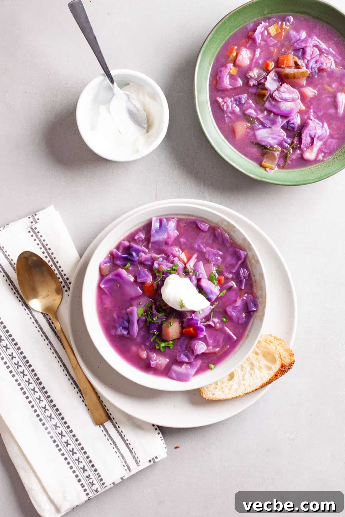 Comforting Red Cabbage Soup Recipe 12 A couple servings of hearty red cabbage soup with one topped with sour cream and fresh herbs and a small bowl of sour cream to the side.