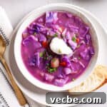 A serving of red cabbage soup in a bowl topped with fresh herbs and sour cream.