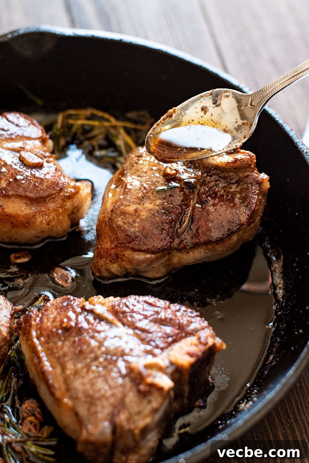 Pan-Seared Lamb Loin Chops with Cognac Butter Recipe 4 A spoon pouring the pan drippings of cognac butter over perfectly seared lamb loin chops in a skillet.