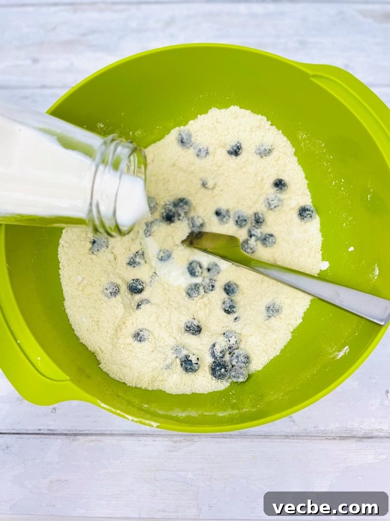 Buttery Blueberry Scones Recipe for Flaky, Tender Results 5 milk being added to blueberry scone mixture in a green bowl