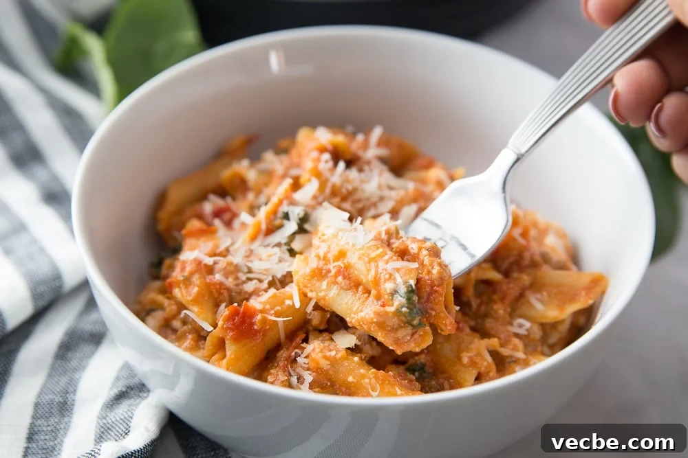 Instant Pot Baked Ziti Recipe 3 White bowl of baked ziti with a hand ready to take a bite with a silver fork