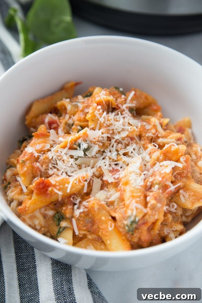 Instant Pot Baked Ziti Recipe 6 Close-up of a white bowl with baked ziti topped with cheese sitting on a blue and white striped kitchen towel