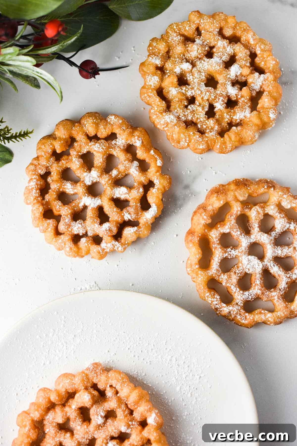 Crispy Rosette Cookies Recipe 4 Three rosettes on a table with powdered sugar on top and a plate nearby.