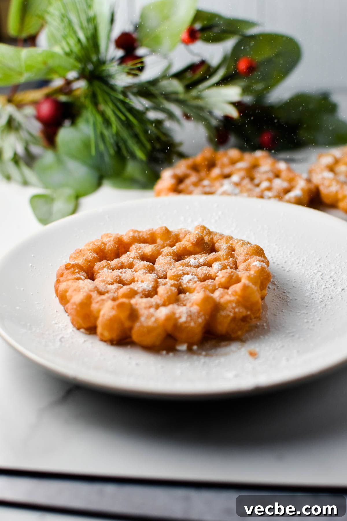 Crispy Rosette Cookies Recipe 6 A snowflake cookie on a white plate being dusted with powdered sugar