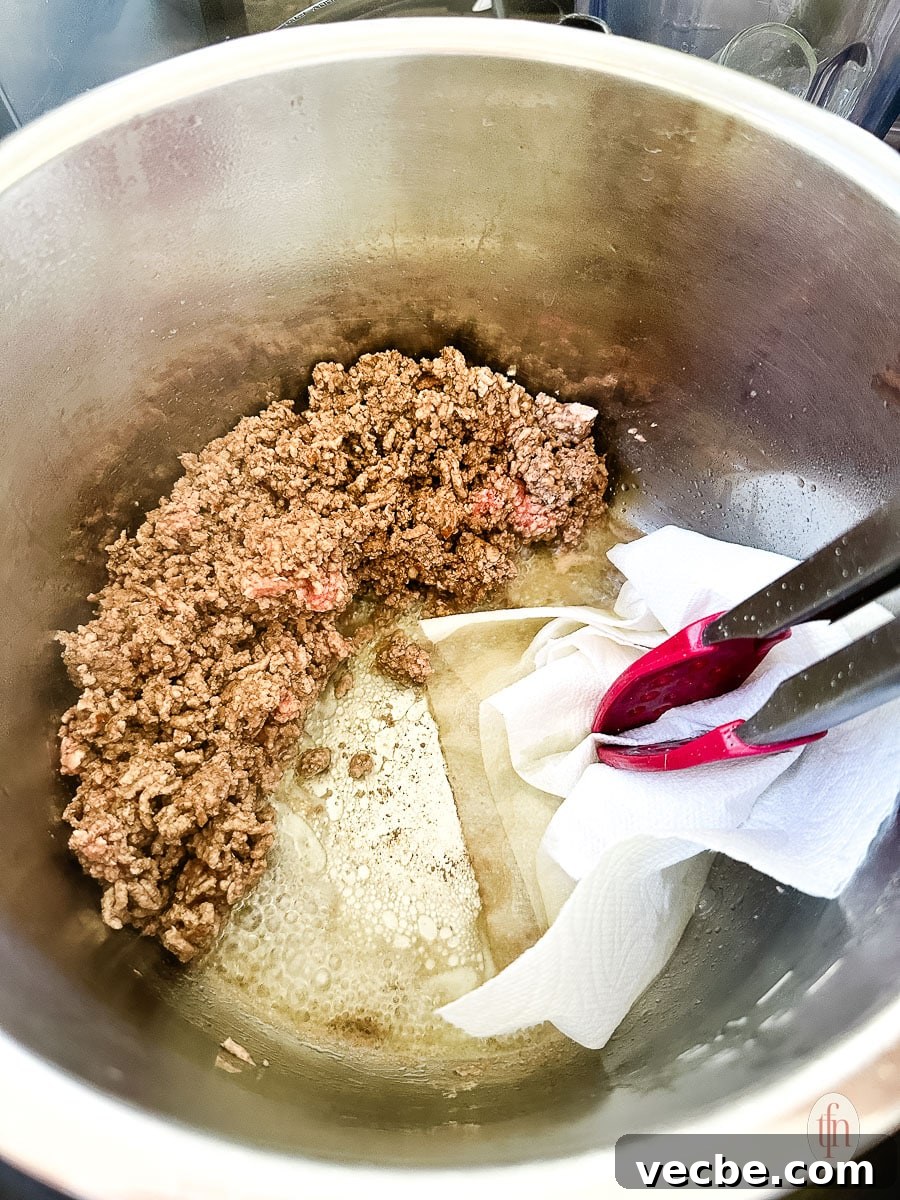 Instant Pot Spaghetti Bolognese Recipe 3 Tongs holding a paper towel to absorb the fat rendered from the sautéed ground beef.