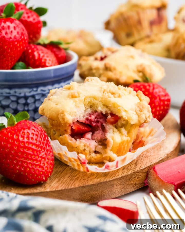 Strawberry rhubarb muffins on a table with a bowl of strawberries.