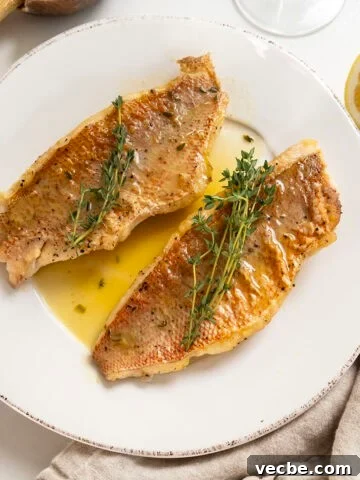 2 filets of pan seared vermillion snapper on a plate garnished with thyme sprigs.