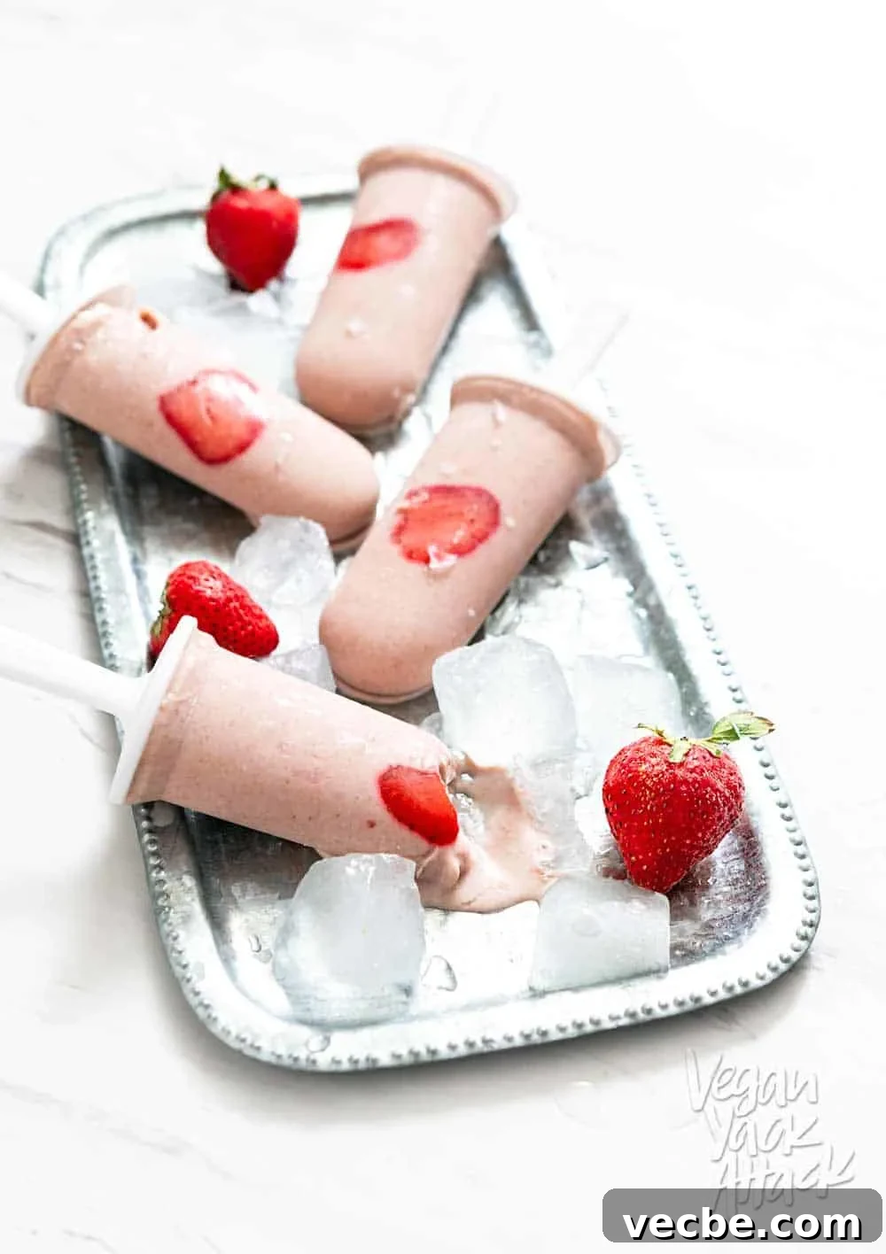 Creamy Strawberry Oat Milk Popsicles Recipe 8 Strawberry Oat Milk Popsicles on a metal platter with ice cubes