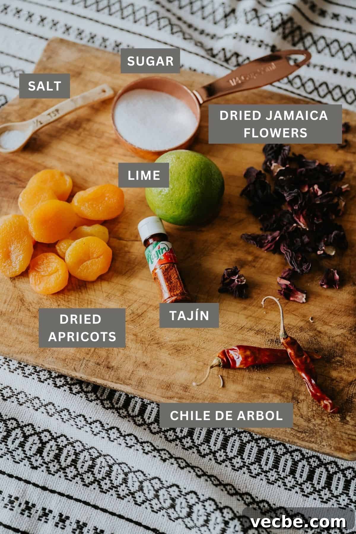 How to Make Mexican Chamoy Sauce at Home 5 Ingredients for a homemade chamoy recipe by Yvette Marquez-Sharpnack of Muy Bueno, including dried apricots, dried jamaica (hibiscus), sugar, and seasonings arranged on a wooden board.