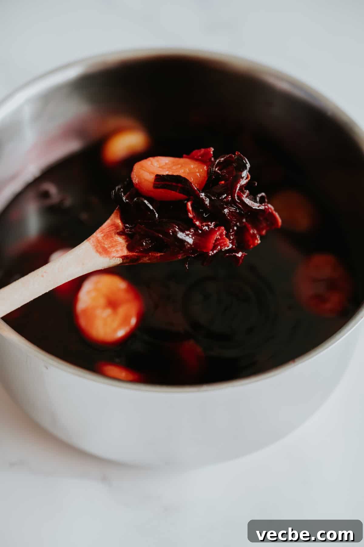 How to Make Mexican Chamoy Sauce at Home 7 Homemade chamoy recipe by Yvette Marquez-Sharpnack of Muy Bueno simmering in a pot, with a wooden spoon showing softened apricots and hibiscus for this sweet, sour, and spicy Mexican chamoy sauce.