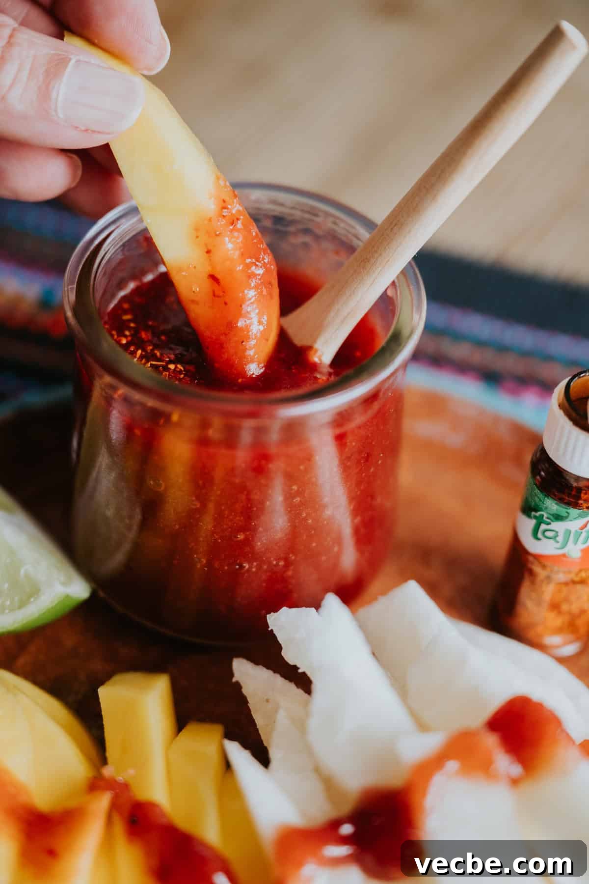 How to Make Mexican Chamoy Sauce at Home 9 Mango slice dipped in a homemade chamoy recipe by Yvette Marquez-Sharpnack of Muy Bueno, a sweet, sour, and spicy Mexican chamoy sauce served in a clear jar with chile lime seasoning, alongside fresh mango and jicama.