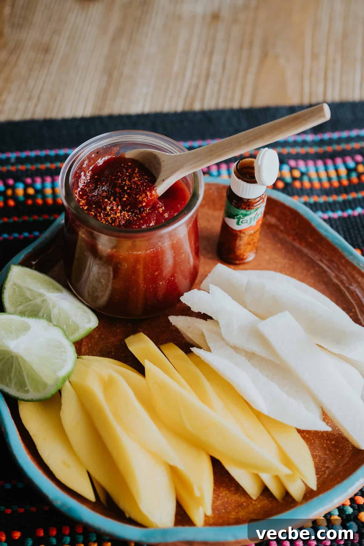 How to Make Mexican Chamoy Sauce at Home 10 Homemade chamoy recipe by Yvette Marquez-Sharpnack of Muy Bueno served in a glass jar with a wooden spoon, topped with chile lime seasoning and paired with fresh mango and jicama.