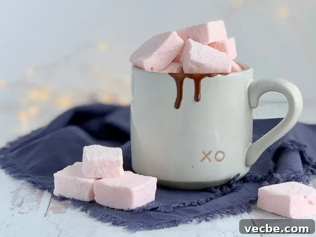 Romantic Valentine's Day Recipes for Two 5 Soft fluffy pale pink square marshmallows on a table next to a mug of hot chocolate.