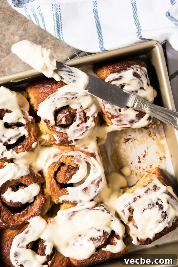 Fluffy Paleo and Keto Cinnamon Rolls Recipe with Yeast 6 Smearing glaze on keto cinnamon rolls in gold baking pan