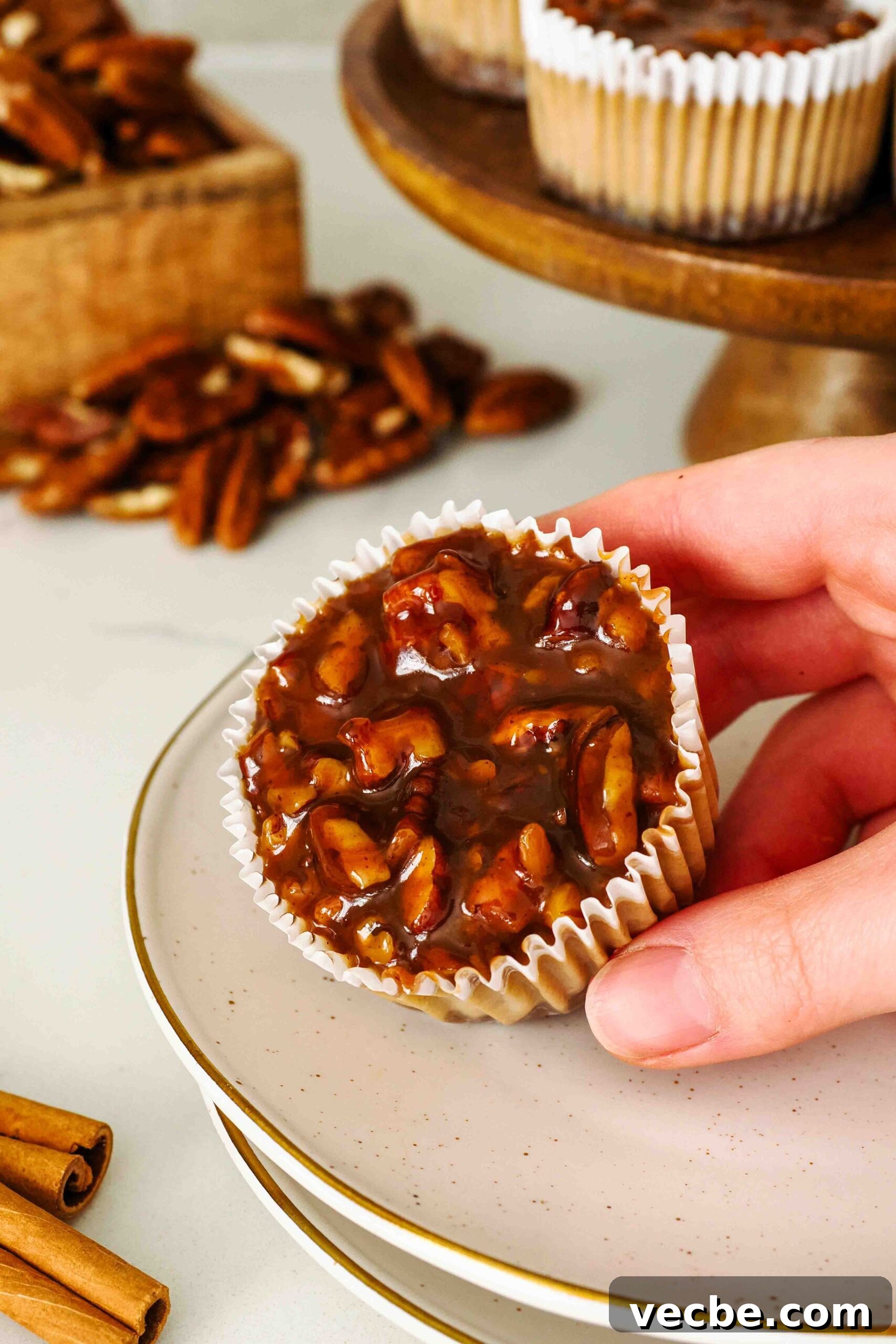 Mini Pecan Pie Cheesecake Bites Recipe 2 A hand holds a mini pecan pie cheesecake at an angle on a dessert plate.